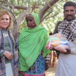 Nolin, a Christian missionary, stands with a Marwari couple receiving a food bag, flanked by a police officer and a volunteer military member from the church who now serves as security for the Bible College in Pakistan.