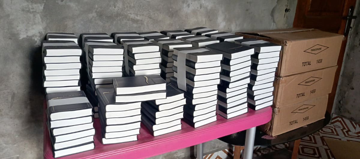 Stacks of Bibles neatly arranged on a table, ready for distribution in the Democratic Republic of Congo (DRC), with boxes labeled "Francophone TOTAL 1459" in the background.