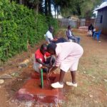 Two people in Kenya using water from a faucet that is run from the new well.