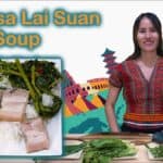 A smiling woman in traditional Chin tribal clothing stands next to ingredients for "Vawksa Lai Suan," a pork soup meal. In the foreground, there is a plate of rice, pork belly, and greens, alongside colorful landmarks representing global culture.