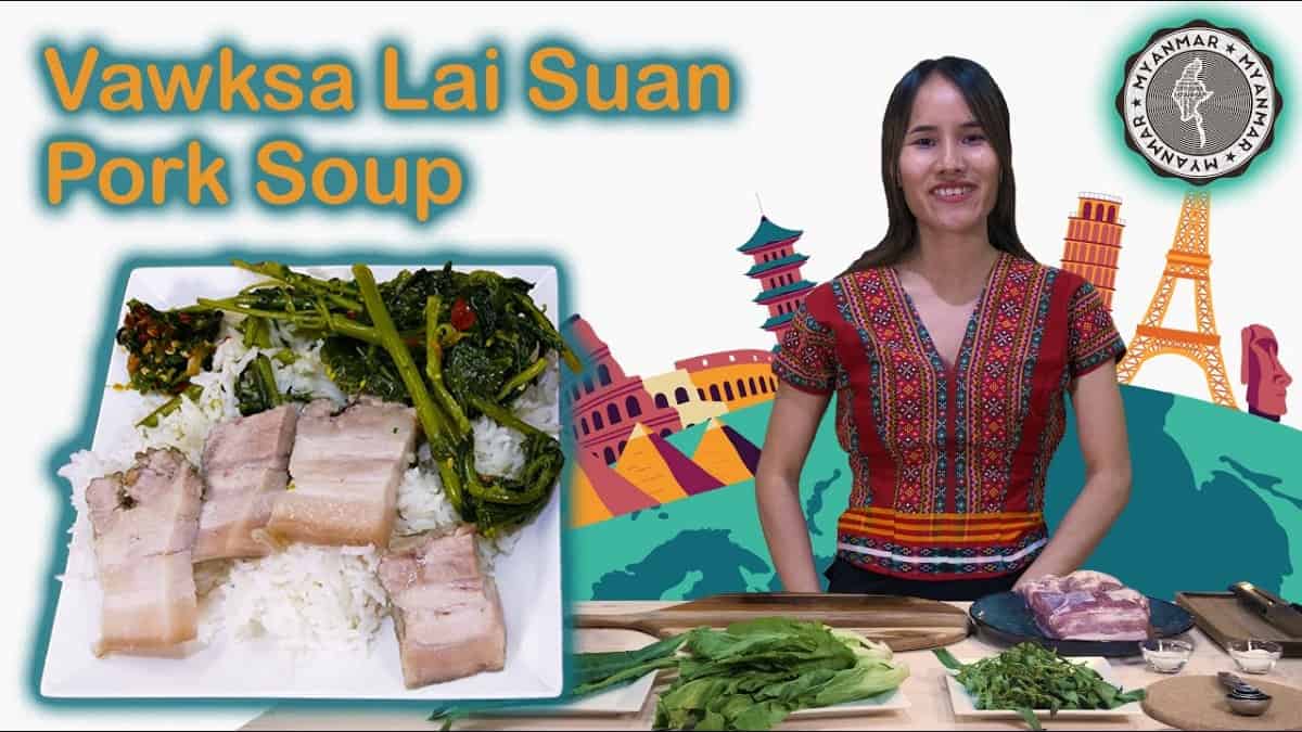 A smiling woman in traditional Chin tribal clothing stands next to ingredients for "Vawksa Lai Suan," a pork soup meal. In the foreground, there is a plate of rice, pork belly, and greens, alongside colorful landmarks representing global culture.