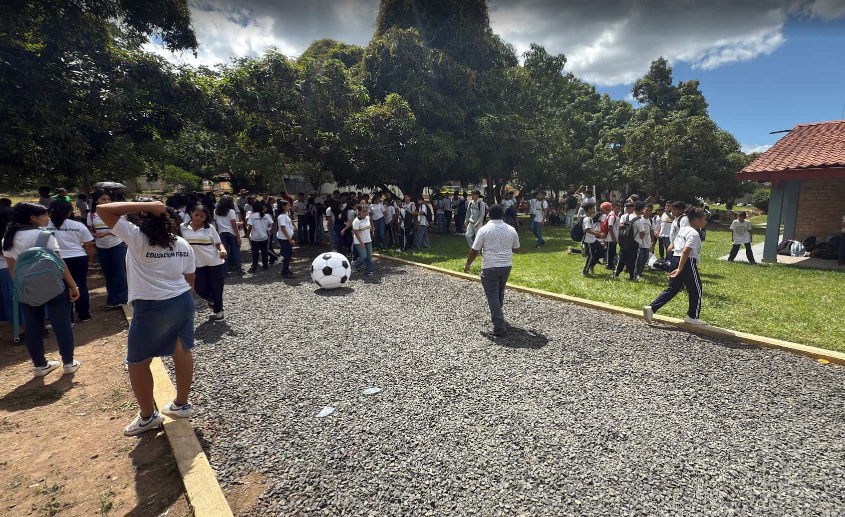 Students gathered outdoors at a school, preparing for a soccer activity under the shade of trees.