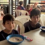 Two boys, 8 and 10 years old, sitting at a table, each with a bowl or arroz con leche.